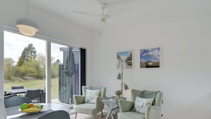 A modern living room with a dining area, featuring a large window, a ceiling fan, and two framed pictures on the wall. - "Wehrhart" - 200m from the sea by Interhome (Væggerløse)