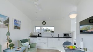 A modern kitchen with white cabinets, a dining table with chairs, a small side table, and a ceiling fan. - "Wehrhart" - 200m from the sea by Interhome (Væggerløse)