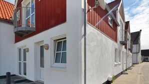 Une rangée de bâtiments blancs rehaussés de touches de rouge, avec des balcons, des fenêtres et une rue pavée.