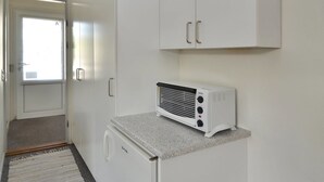 Une cuisine dotée d’un four à micro-ondes encastré, d’un plan de travail en granit, de meubles blancs et d’une porte donnant sur une autre pièce.