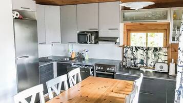 Ett kompakt kök med ett matbord i trä, ett kylskåp, en mikrovågsugn och en spis.