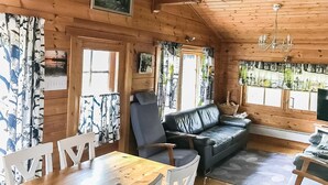 L’intérieur d’un chalet en bois, avec un canapé, des fauteuils, une table et un lustre.