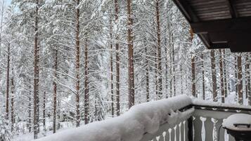 Un balcone innevato con ringhiera, affacciato su una fitta foresta di alberi carichi di neve.