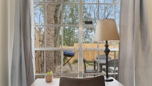 Une pièce dotée d’une grande fenêtre, d’une table avec une lampe et donnant sur le jardin arrière.