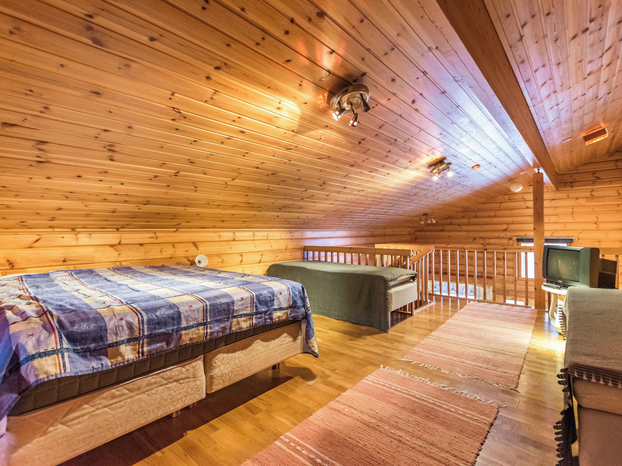Une chambre dans un chalet en rondins, avec un lit, un canapé, une télévision et un plafond en bois.