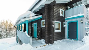 Una cabaña de madera con porche y una puerta oscura, rodeada de nieve.