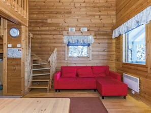 A wooden cabin interior with a red sofa, a clock, a map, and a window with a view of trees. - Rakotuli 2 paritalon yläkerta by Interhome (Hyrynsalmi)