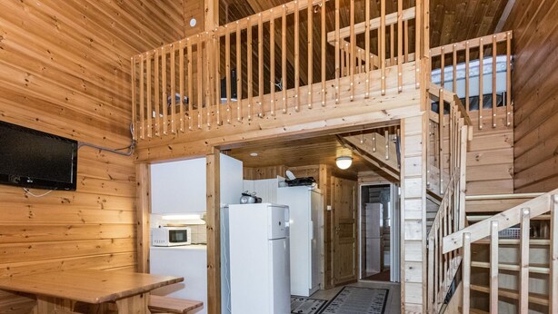 Interior de una cabaña de madera con comedor, cocina y una escalera que sube a un altillo.