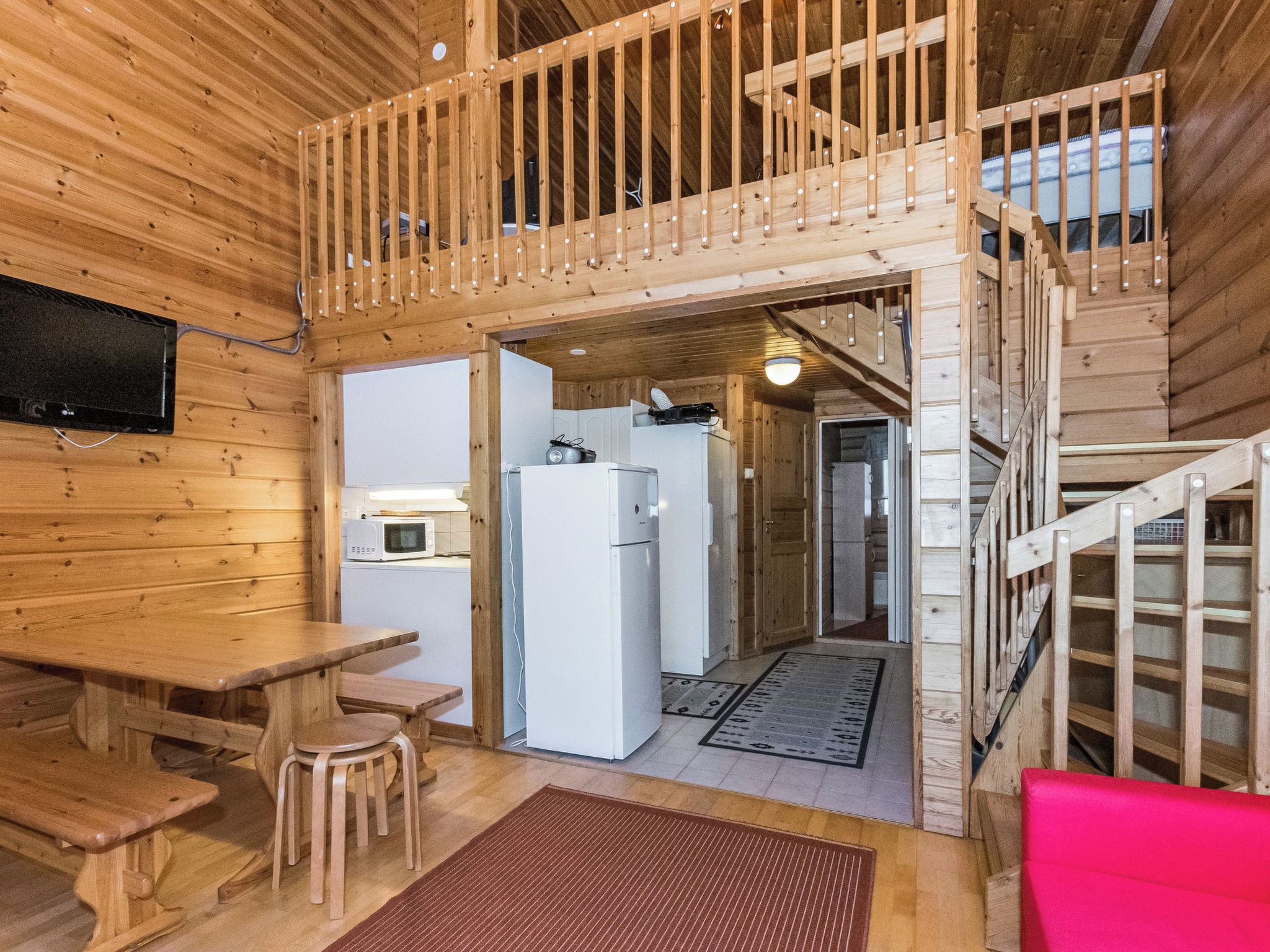 Interior de uma cabana de madeira com área de refeições, cozinha e escada para um andar superior.