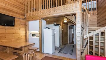 Interior de uma cabana de madeira com área de refeições, cozinha e escada para um andar superior.