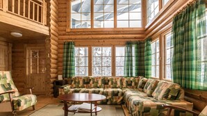 A log cabin interior with a large window, a wooden ceiling, and a green plaid sofa. - Aurinkoinen hirsimökki by Interhome (Hyrynsalmi)
