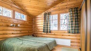 A cozy log cabin bedroom with a bed, two windows with plaid curtains, and a radiator under the window. - Aurinkoinen hirsimökki by Interhome (Hyrynsalmi)