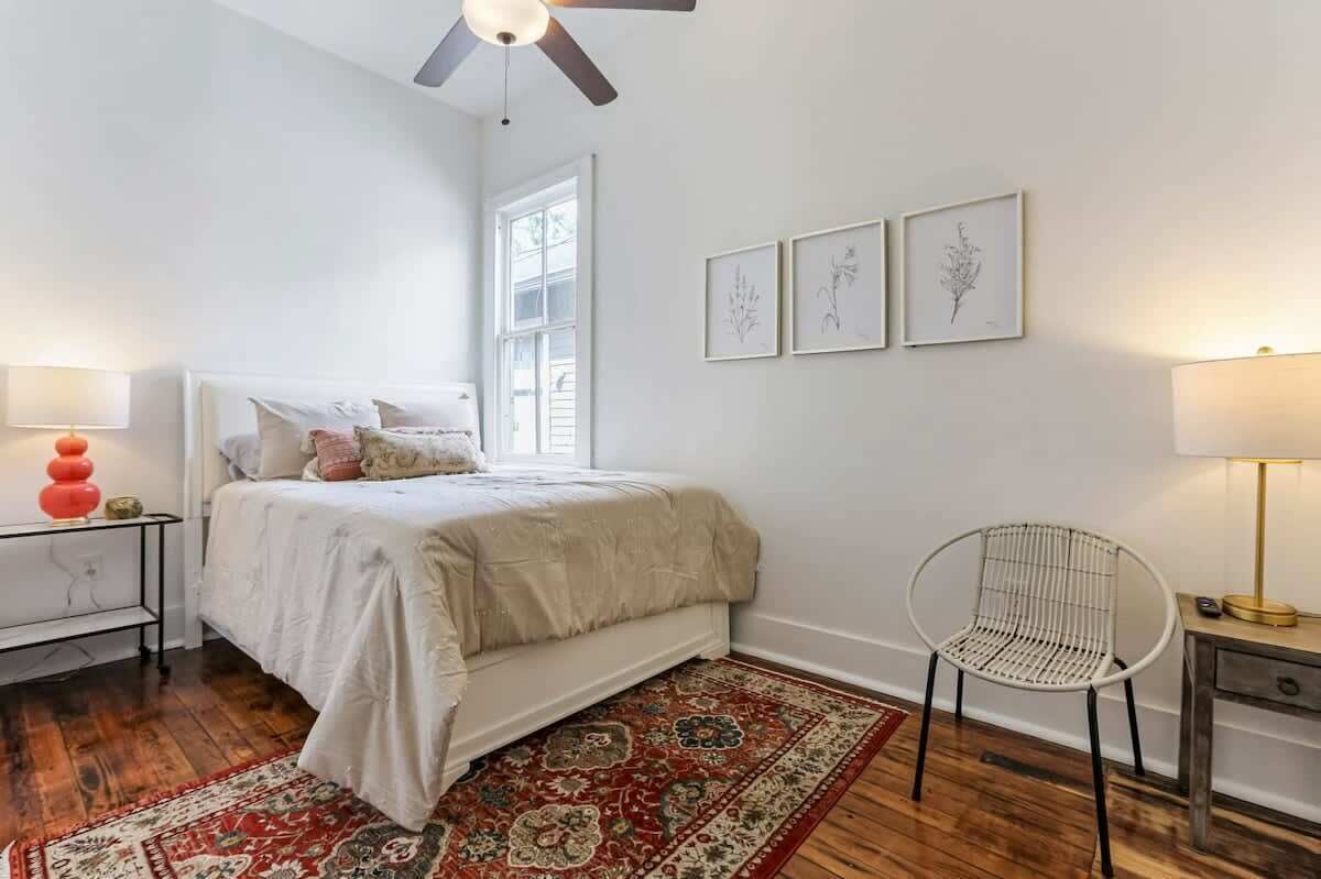 Quarto com cama, uma cadeira, mesa de cabeceira, abajur e ventilador de teto.