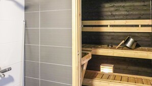 A bathroom with grey tiled walls, a shower, and wooden shelves with a pot and a box. - Skivillas 47 ukkohalla (a1) by Interhome (Hyrynsalmi)