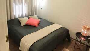 A bedroom with a bed, curtains, a bedside lamp, and a small table with a lamp. - Skivillas 47 ukkohalla (a1) by Interhome (Hyrynsalmi)