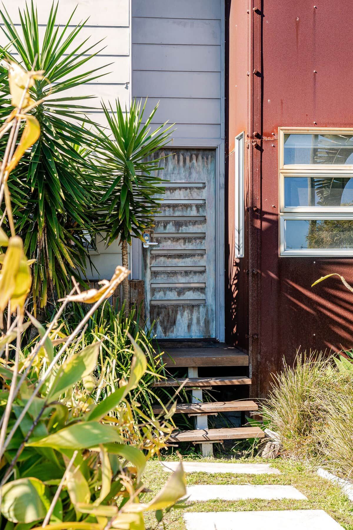 A house with a wooden staircase leading to a door, surrounded by various plants.