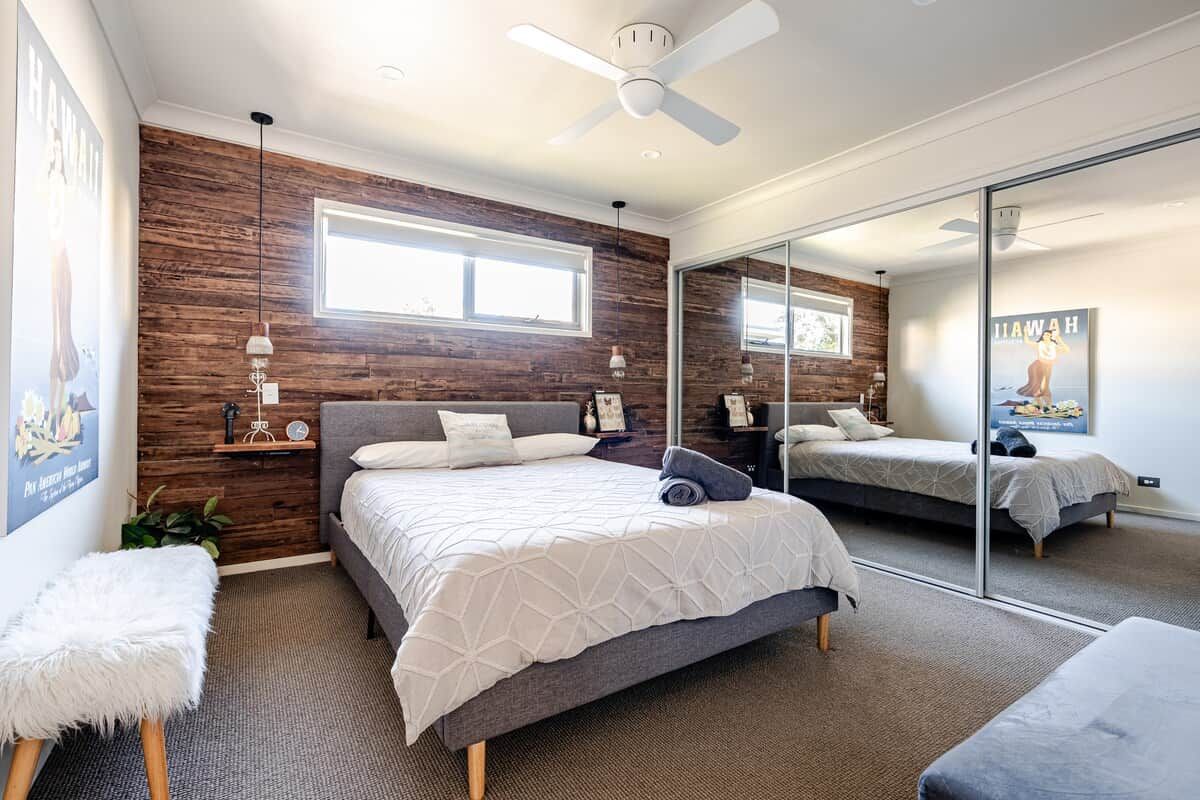 A bedroom with a large bed, a bedside table, a mirror, and a ceiling fan.