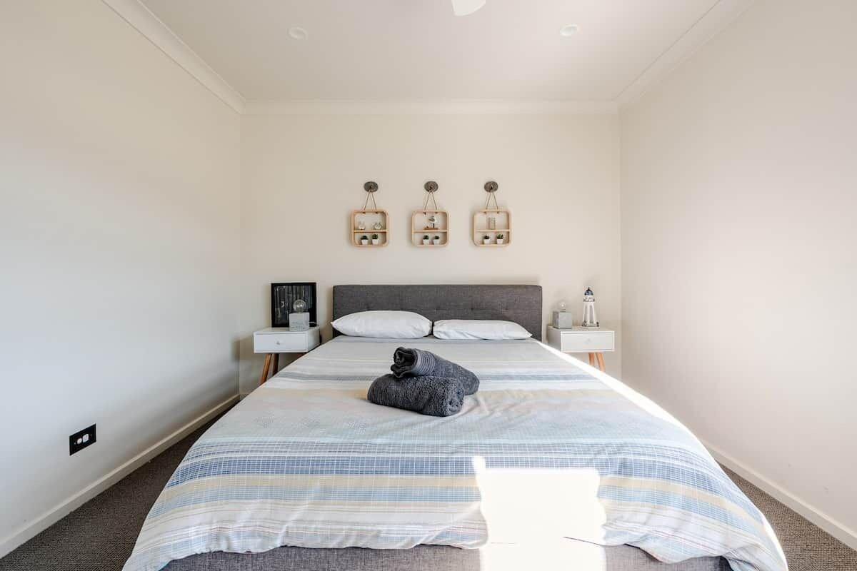 A bedroom with a bed, two bedside tables, and three wall-mounted light fixtures.
