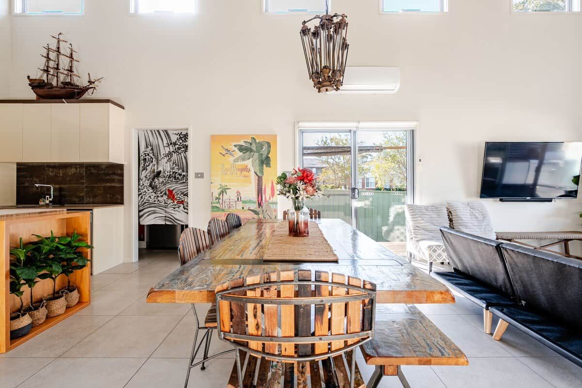 A spacious living area with a long wooden dining table, a comfortable sofa, and a television mounted on the wall.
