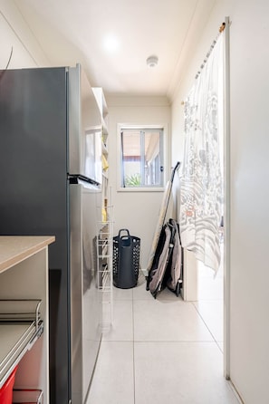 A compact kitchen with a refrigerator, a small window, and a view of the outside. - The Wharf House @ Sussex Inlet (Sussex Inlet)