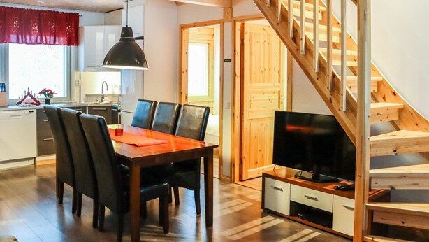 A modern kitchen with a dining area, wooden staircase, and a TV in a cozy living space.