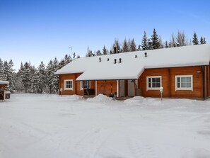 Cozy cabin with a front porch and chimney, nestled among snow-covered trees.