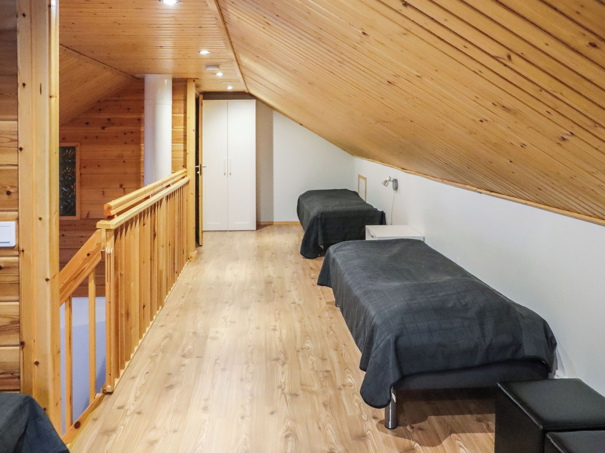 A room with a sloped ceiling, wooden flooring, a staircase, and two beds with dark bedding.