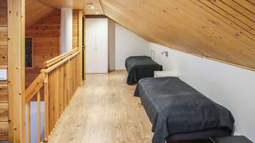A room with a sloped ceiling, wooden flooring, a staircase, and two beds with dark bedding.