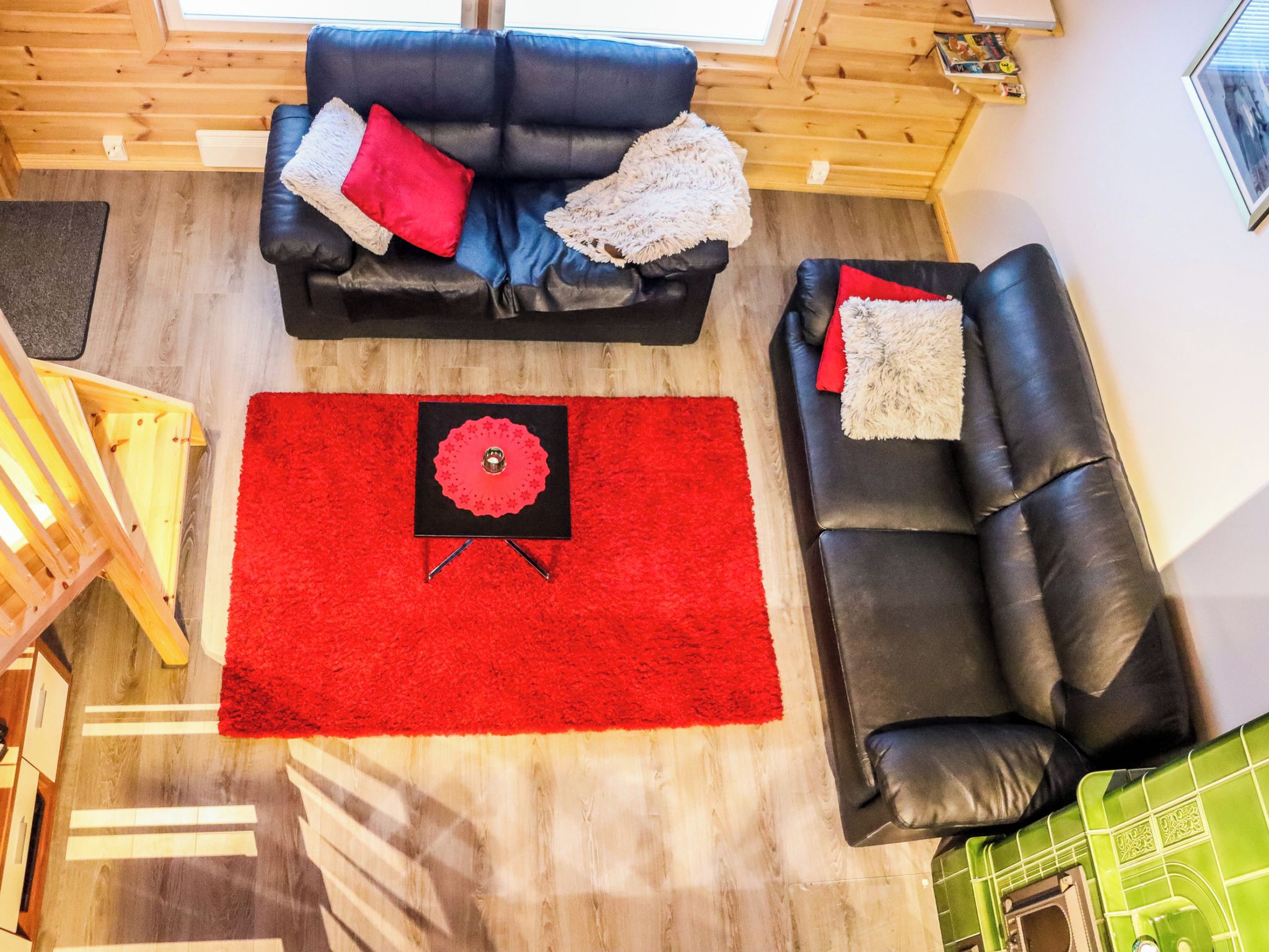 Une pièce avec un canapé en cuir noir, un tapis rouge et un plancher en bois.
