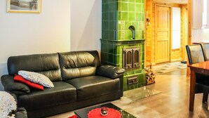 A cozy living room with a green tiled fireplace, a black leather sofa, and a dining table.