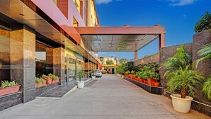 En moderne hotelindgang med et overdækket gelænder, plantekasser og en klar himmel.