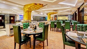 En moderne restaurant med grønne polstrede stole, et centralt barområde og et loft med unikke gyldne detaljer.