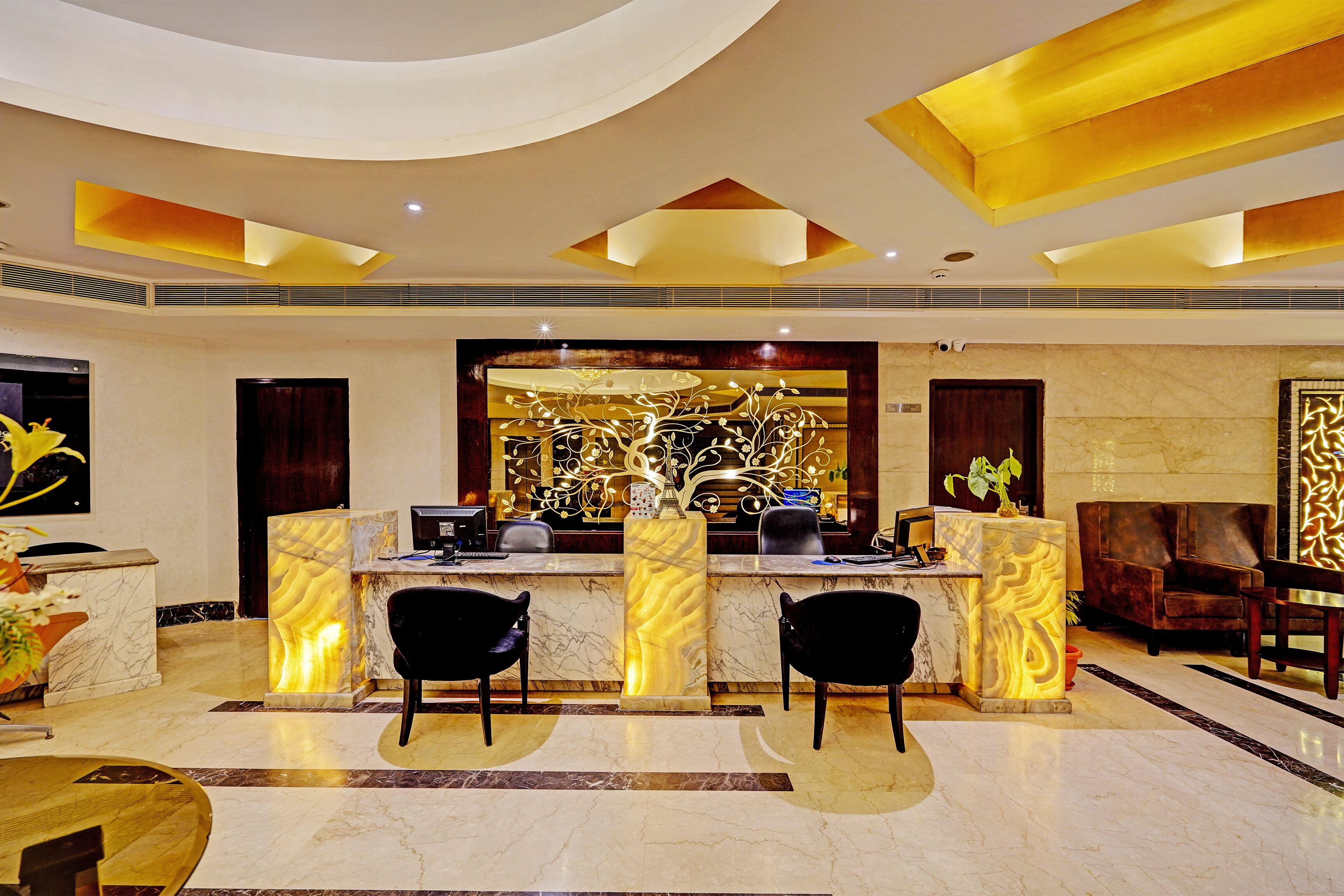Een moderne lobby met een receptiebalie, twee zwarte stoelen, een marmeren vloer en een decoratieve wand.
