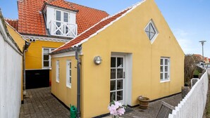 Een geel gebouw met een rode pannendak, een klein balkon en een deur met een bordje.