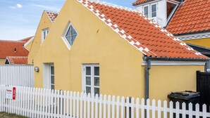 Een geel huis met een witte picket fence, een dak met rode tegels en een klein raam.