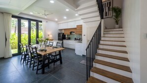 A modern kitchen with white cabinets, a wooden island, and a dining area with a table and chairs. - Villa by Olive - Nerul (Nerul)