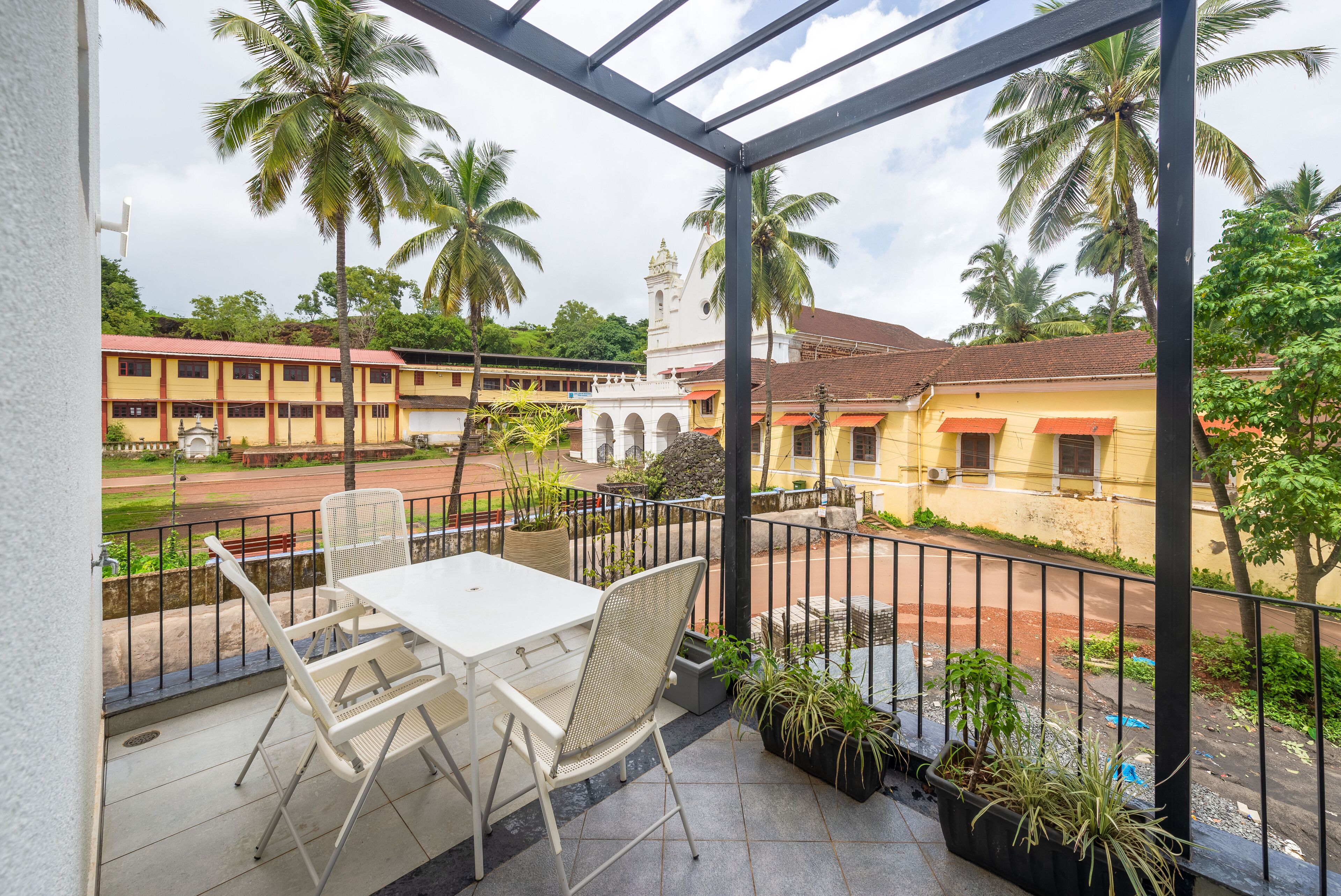 A balcony with a table and chairs, overlooking a street with buildings and palm trees.