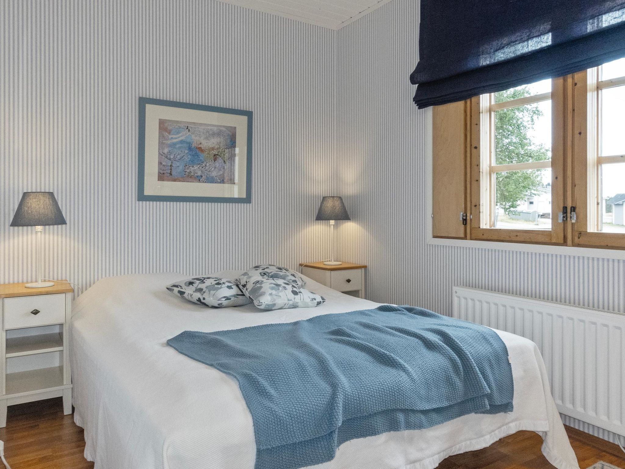 A neatly arranged bedroom with a bed, two bedside tables, a framed artwork, and a window with curtains.