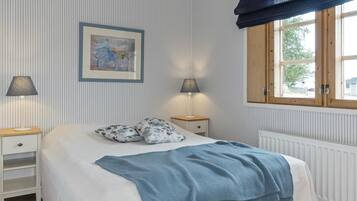 A neatly arranged bedroom with a bed, two bedside tables, a framed artwork, and a window with curtains.