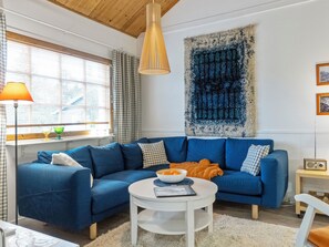 Een moderne woonkamer met een blauwe modulaire bank, een witte salontafel en een groot abstract wandtapijt.