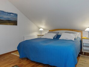 Een slaapkamer met een bed, twee nachtkastjes, een radiator en een schilderij aan de muur.
