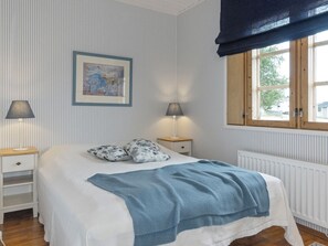 A neatly arranged bedroom with a bed, two bedside tables, a window with a view, and a framed artwork on the wall.