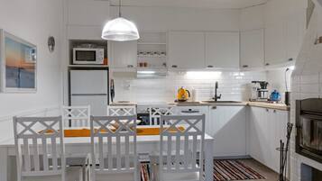 A modern kitchen with white cabinets, a central island with chairs, a hanging light fixture, and a built-in oven.