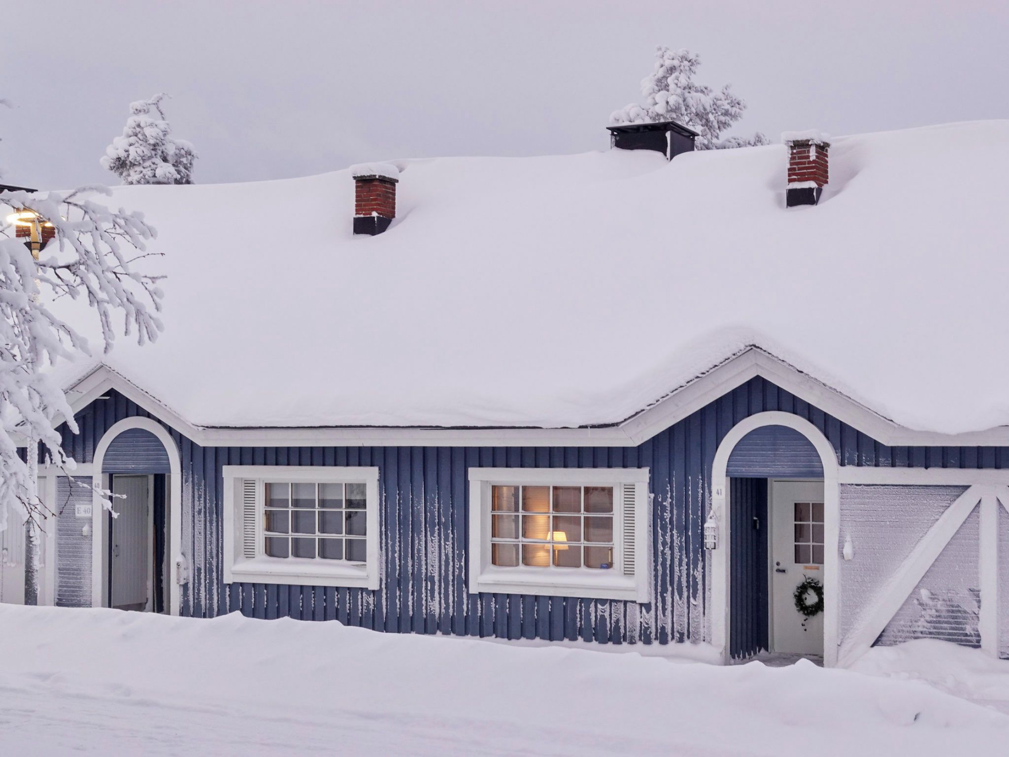 Een huis bedekt met sneeuw, met een blauwe gevel, een voordeur en twee schoorstenen.
