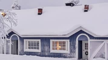 Een huis bedekt met sneeuw, met een blauwe gevel, een voordeur en twee schoorstenen.