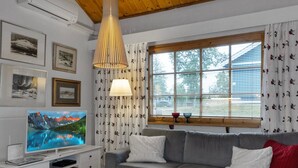 A modern living room with a grey sofa, a flat-screen TV, a white entertainment unit, and a large window with curtains. - Päivänsäde by Interhome (Inari)