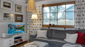 A modern living room with a grey sofa, a flat-screen TV, a white entertainment unit, and a large window with curtains.