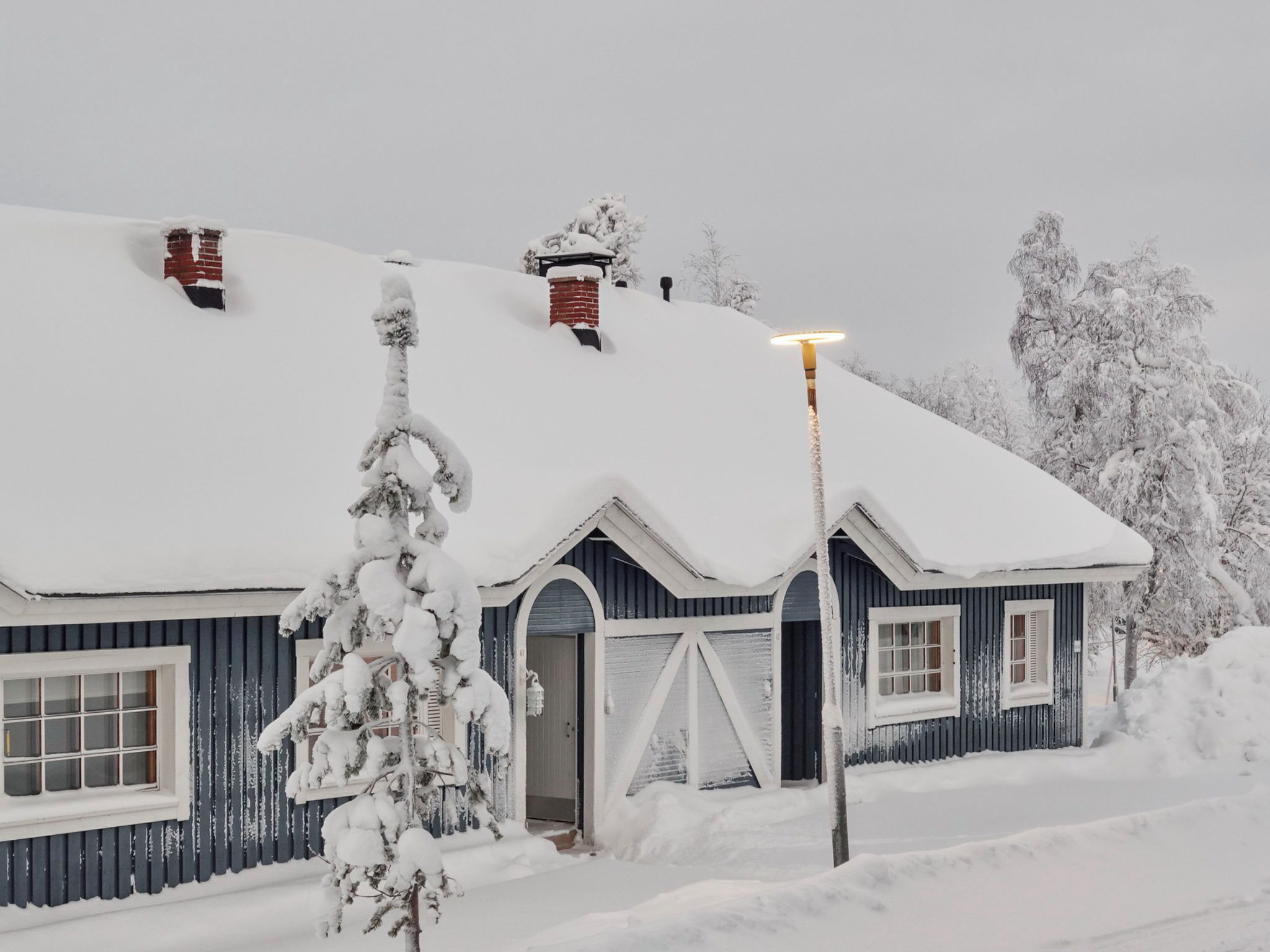 Lumipeitteinen talo, jossa on savupiippu, ovi ja ikkuna.