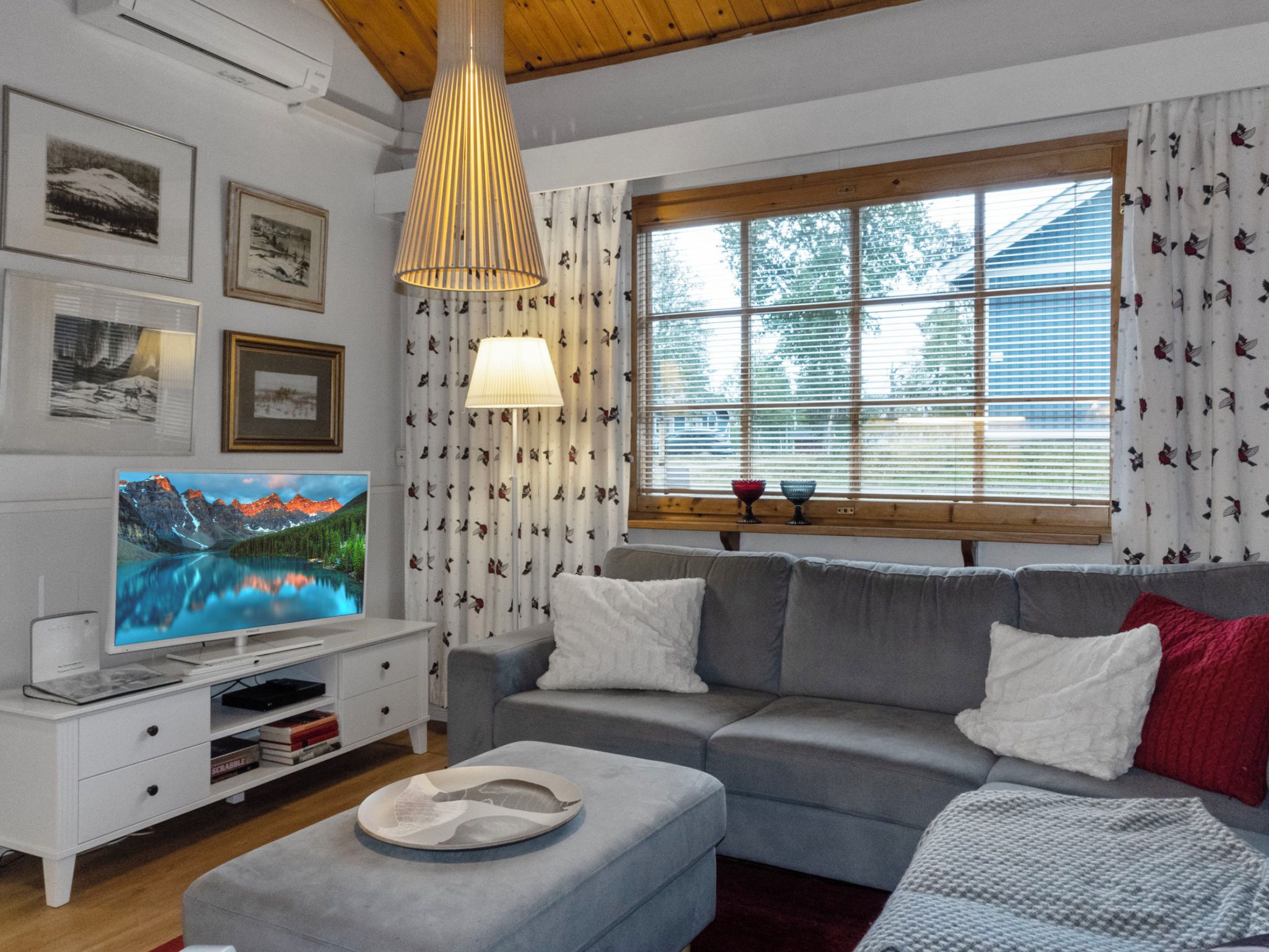 Un salon avec un canapé gris, une table d’appoint blanche, un téléviseur à écran plat et une lampe décorative.