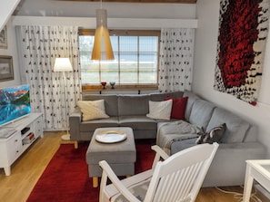 A modern living room with a grey sofa, a white armchair, a red rug, and a television displaying a mountain scene.